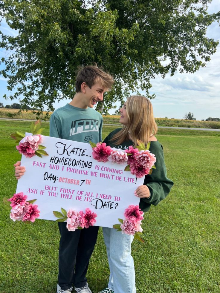 a man and woman holding a sign in the grass with flowers on it that says, kate honeymooning is coming day