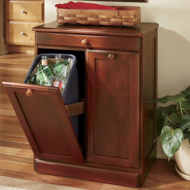 a wooden cabinet with a trash can in it and a mirror on the wall above