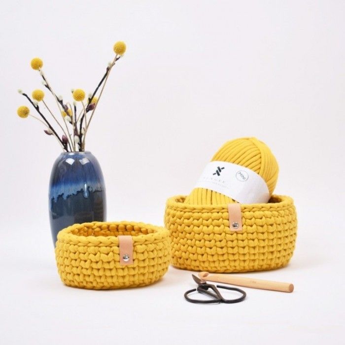 a yellow knitted basket next to a blue vase filled with flowers and knitting needles