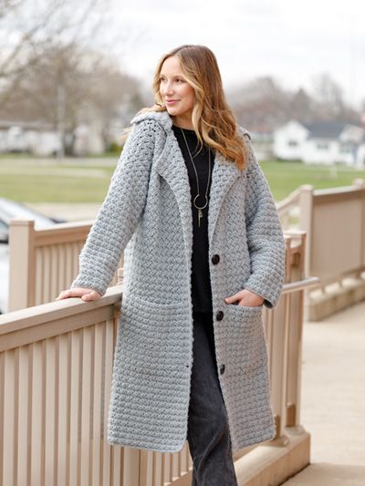 a woman is standing on a bridge wearing a gray coat and black top with her hands in her pockets