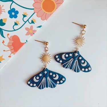 a pair of blue and white butterfly shaped earrings on a floral print tablecloth with pink flowers