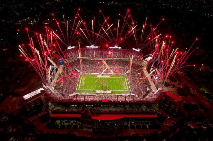 fireworks light up the night sky over an empty football stadium as it is lit up with red and white lights