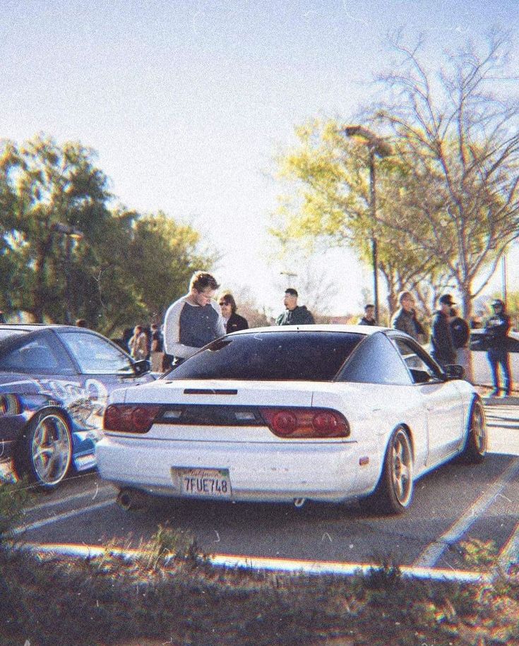 two white cars parked in a parking lot with people standing around them and talking to each other