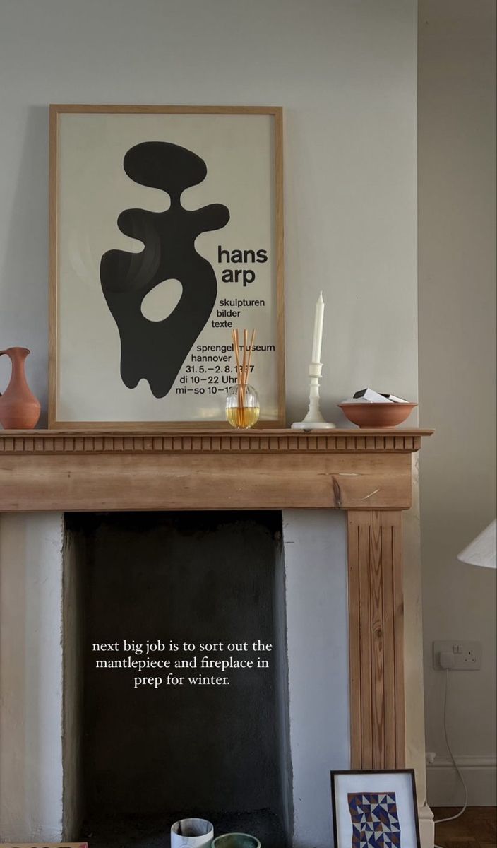 a fireplace mantel with an art print above it and two cups on the mantle