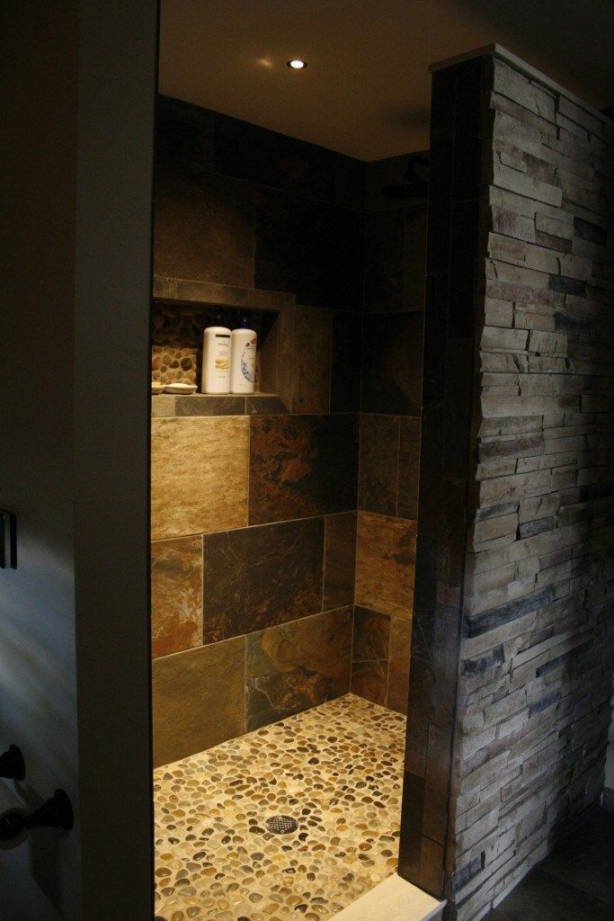 a walk in shower sitting next to a brick wall and tiled floored bathroom area