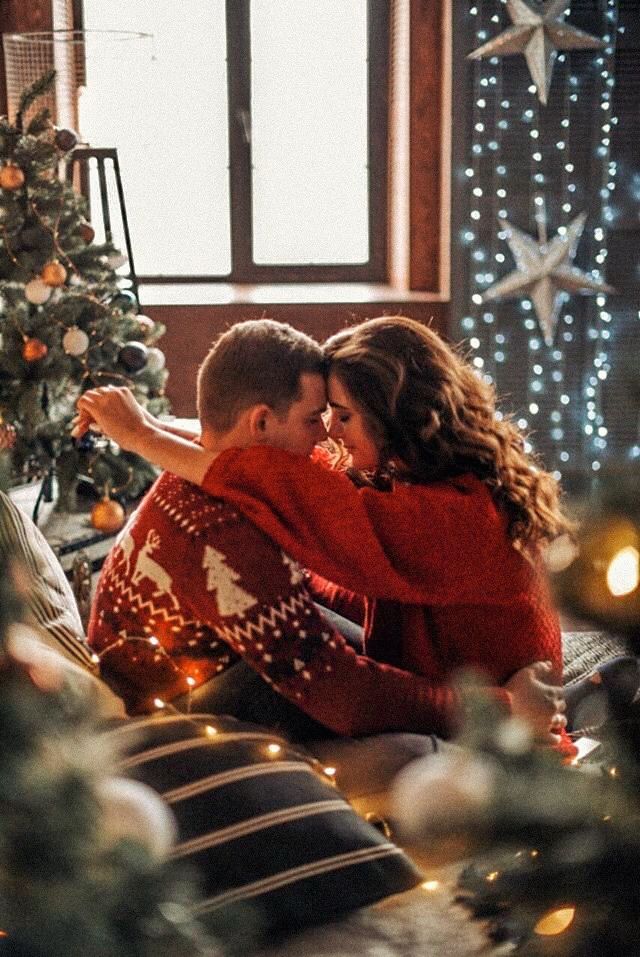 a man and woman sitting next to each other on a couch in front of a christmas tree