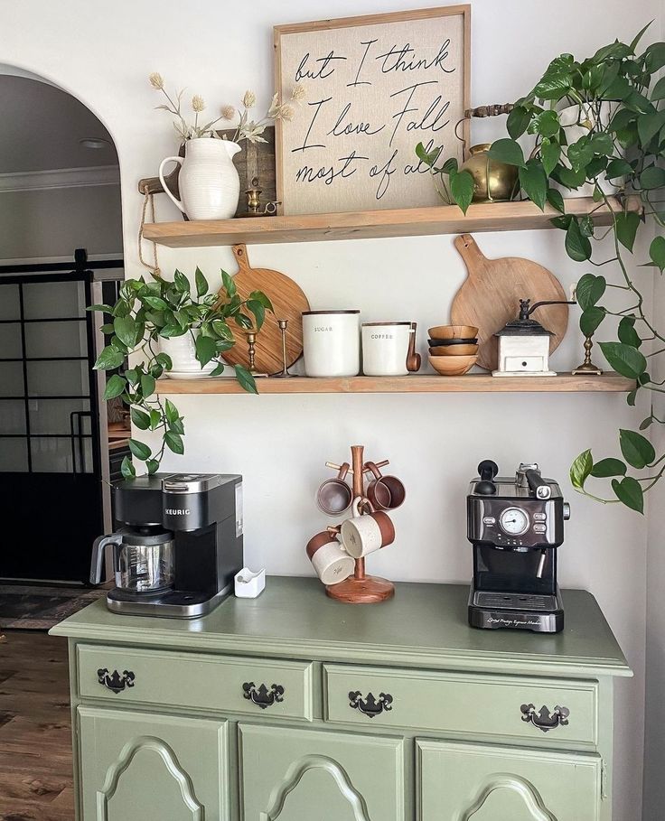 a green cabinet with coffee cups and plants on it in front of a white wall