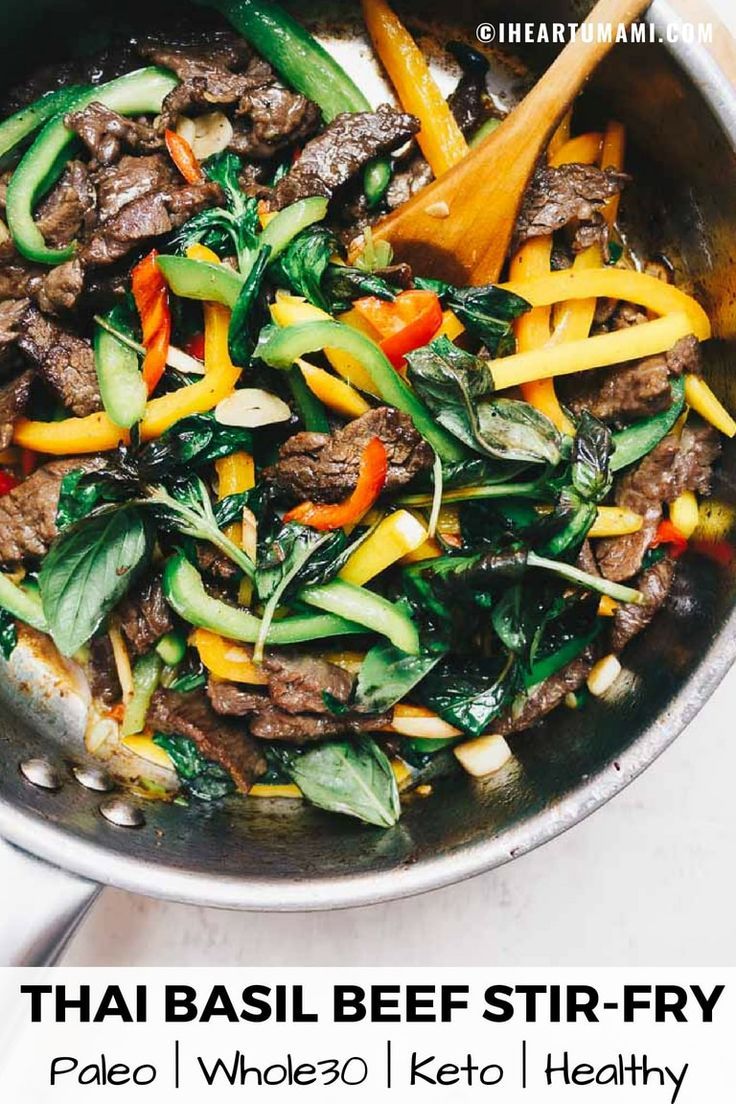 stir fry with meat, vegetables and peppers in a pan on the stove top next to a wooden spoon