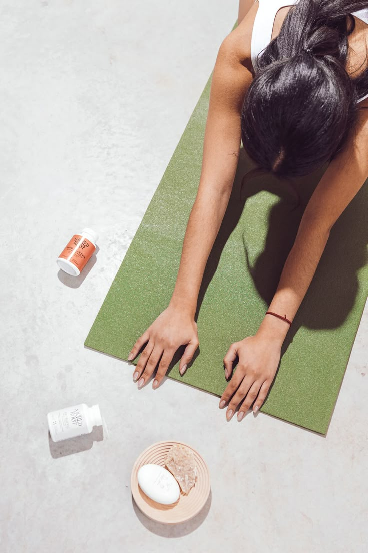 a woman laying on top of a yoga mat with her hands in the air next to a bottle of lotion