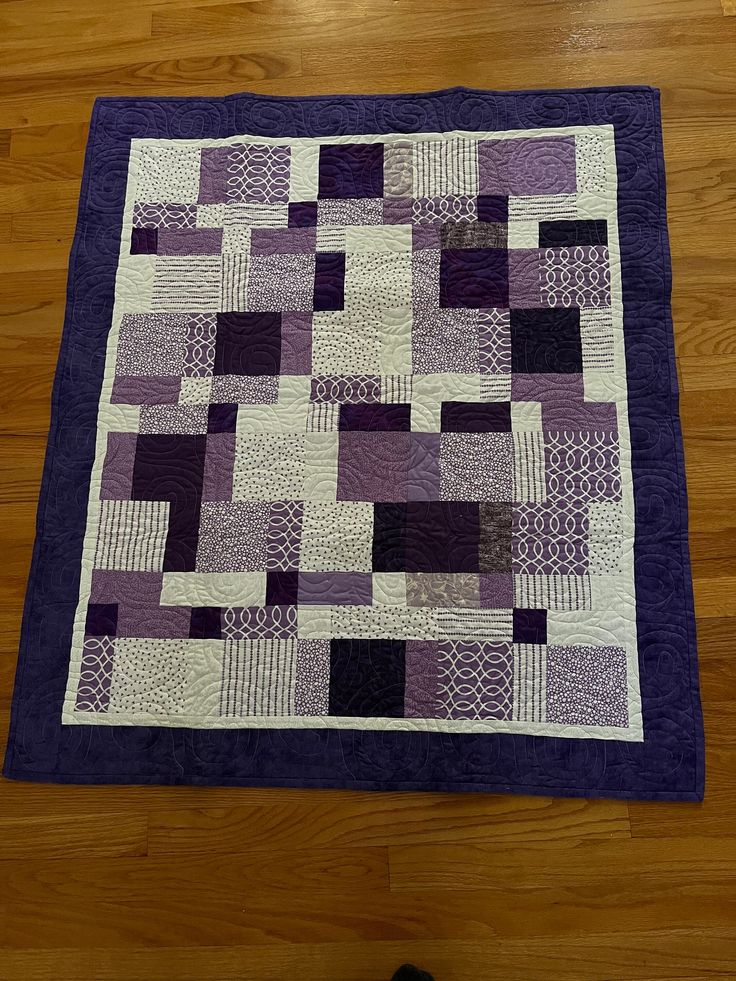 a purple and white patchwork quilt on a wooden floor next to a pair of shoes