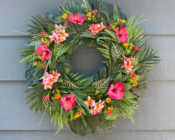 a wreath with pink flowers and green leaves hanging on the side of a house wall