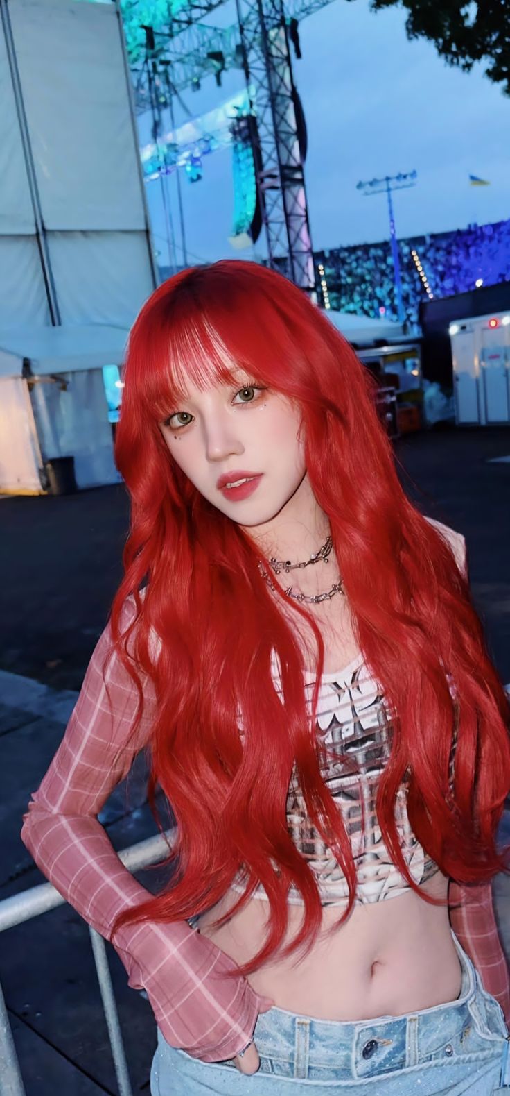 a woman with long red hair standing next to a fence