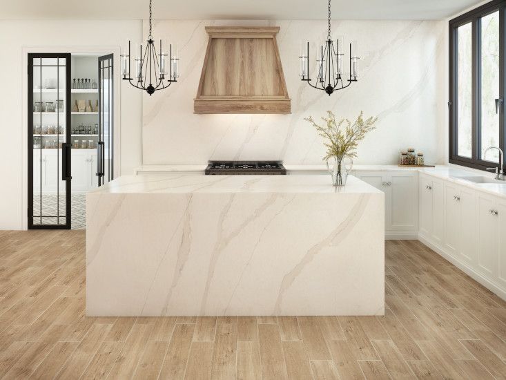 a kitchen with white marble counter tops and wooden flooring that has chandeliers hanging from the ceiling