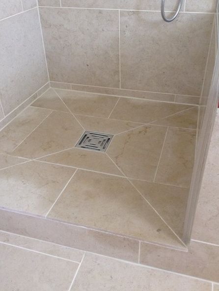 a shower stall with a drain in the middle and tiled flooring on both sides