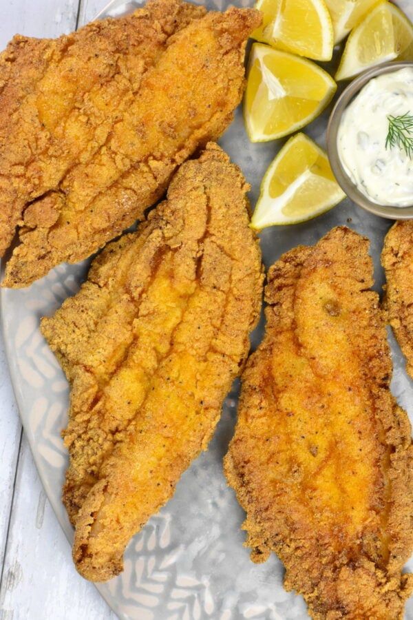 fried fish and lemon wedges on a plate with ranch dip in the middle next to it