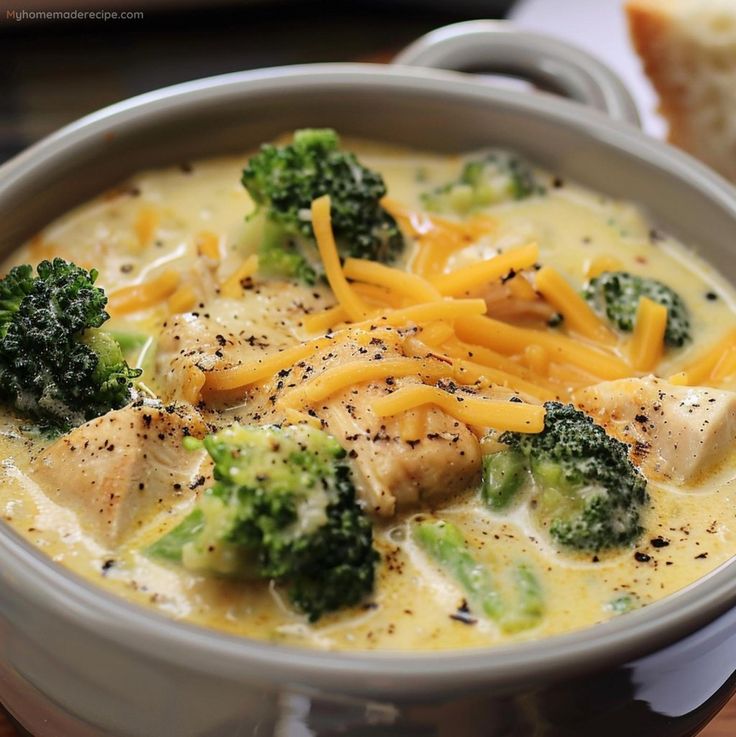 a bowl of broccoli and cheese soup on a wooden table with bread in the background