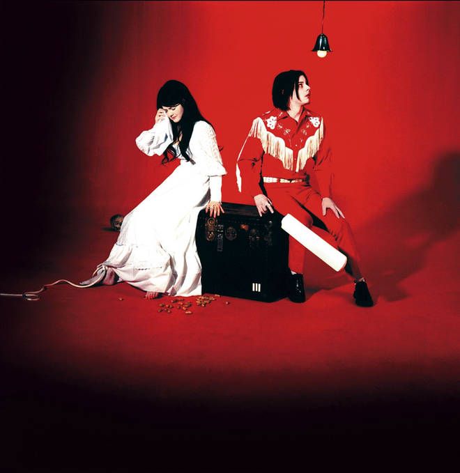 two people sitting on top of a piece of luggage in front of a red background