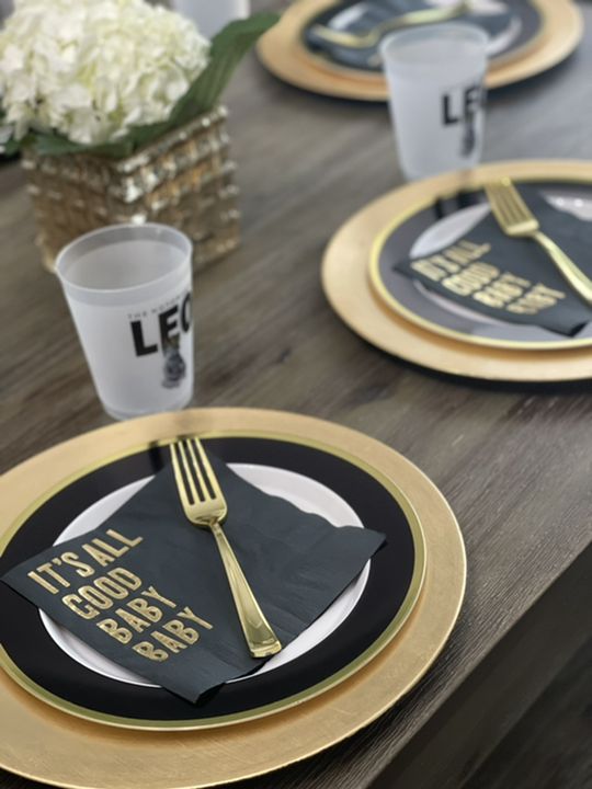 the table is set with black and gold plates, silverware, and white flowers