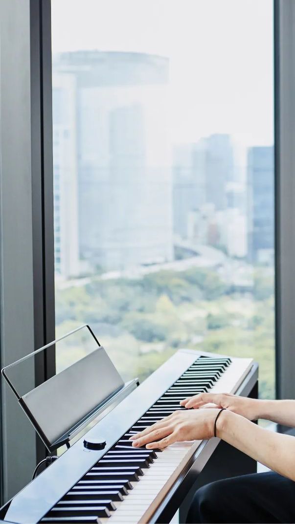 a woman sitting at a piano with her hands on the keyboard and looking out the window