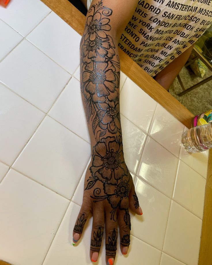 a woman's arm with tattoos on it sitting on a tiled floor next to a table