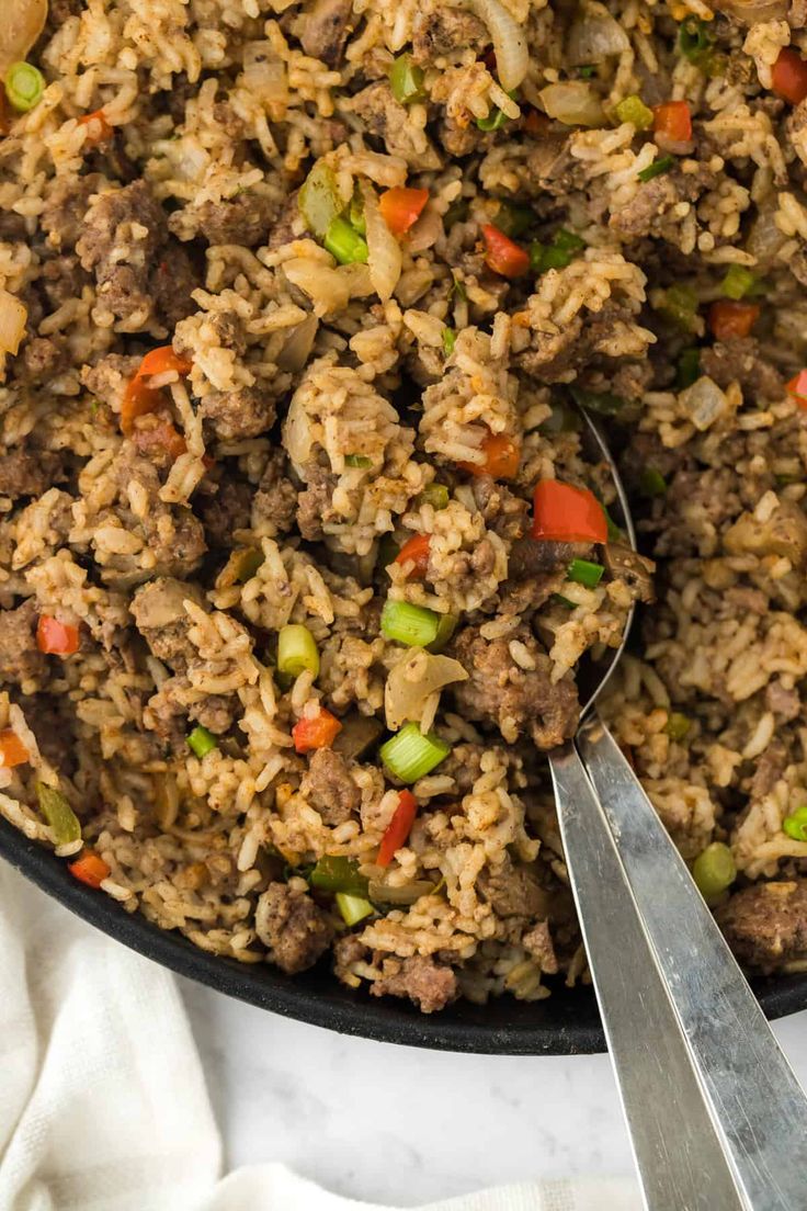 a skillet filled with rice and meat on top of a white cloth next to two spoons