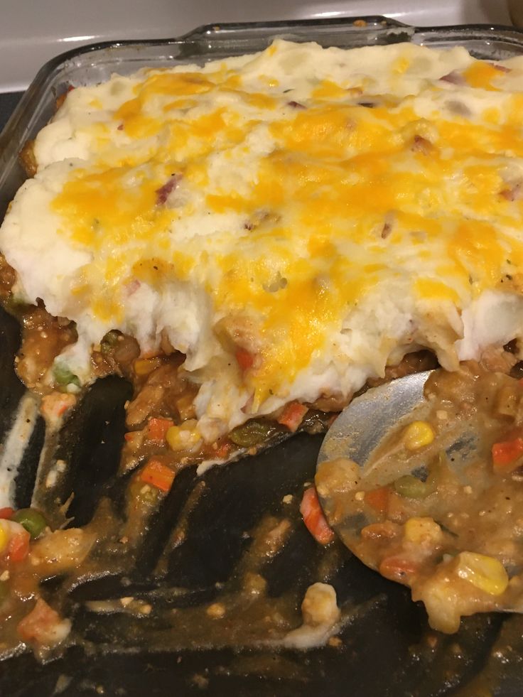 a casserole dish with meat, vegetables and cheese on top is being lifted from the oven