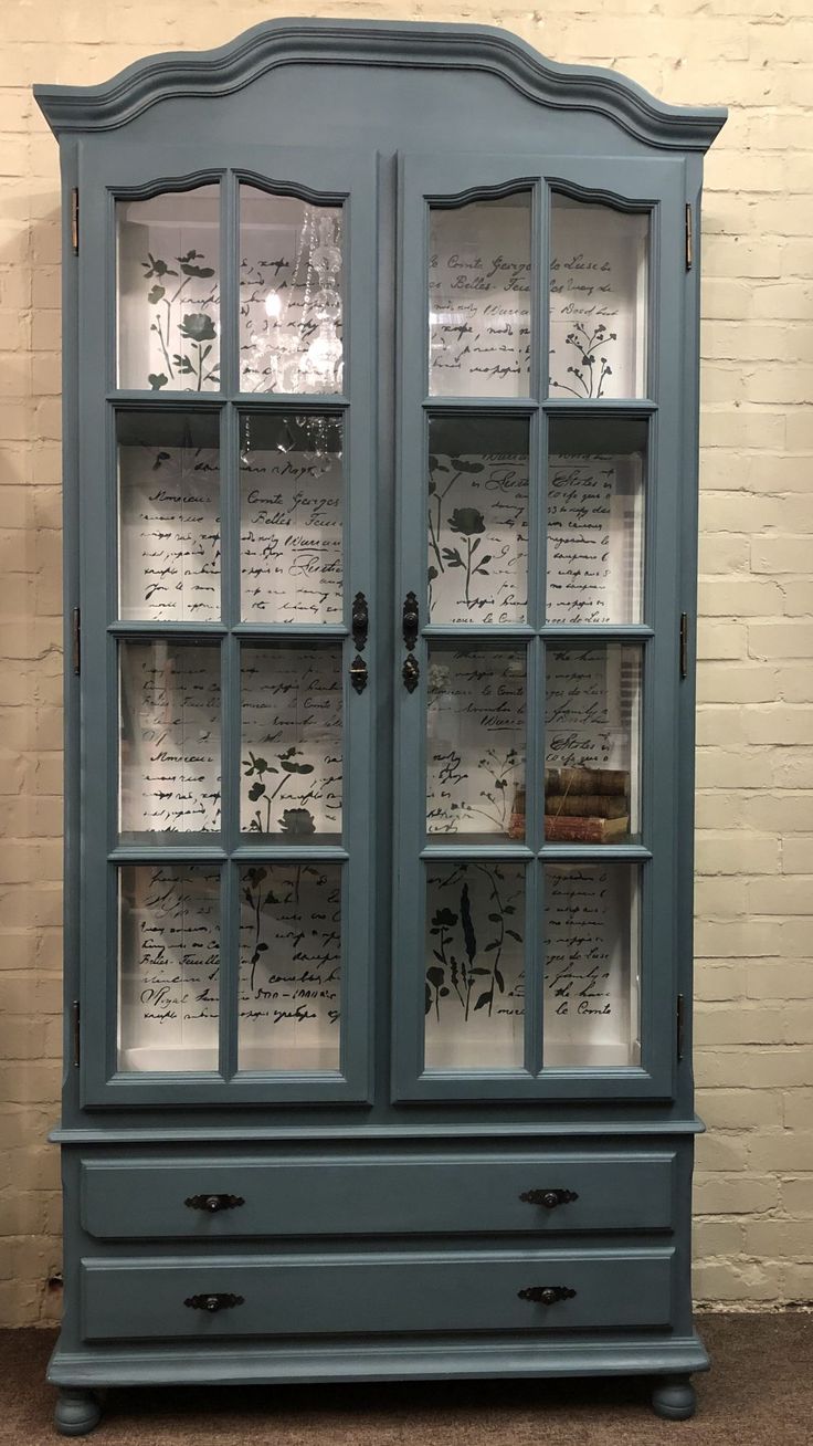 a blue china cabinet with writing on the glass doors and drawers in front of it