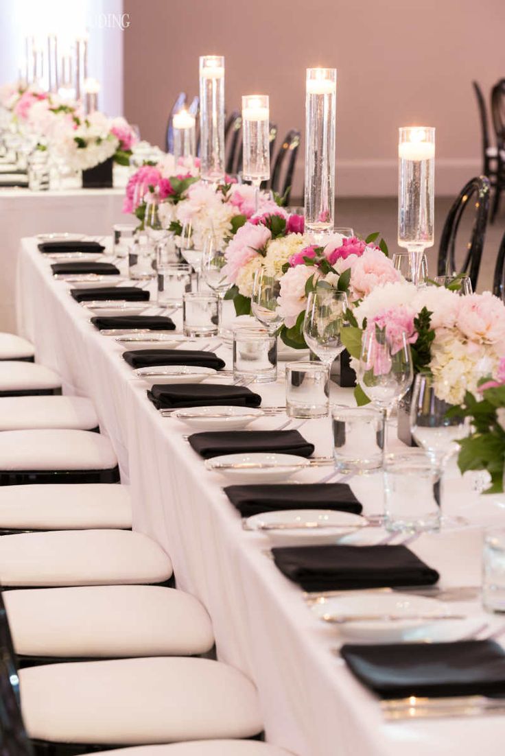 a long table is set with black and white place settings, candles, and flowers