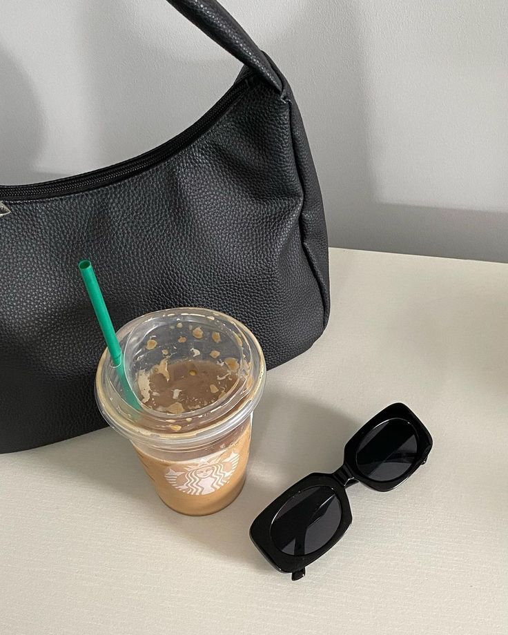 a cup of coffee and sunglasses sitting on a table next to a black purse,