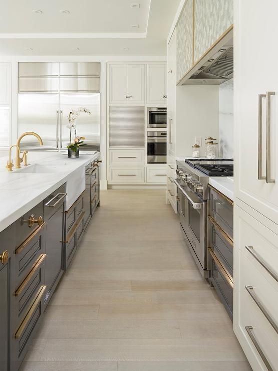 a large kitchen with white cabinets and gold handles on the countertops, along with stainless steel appliances