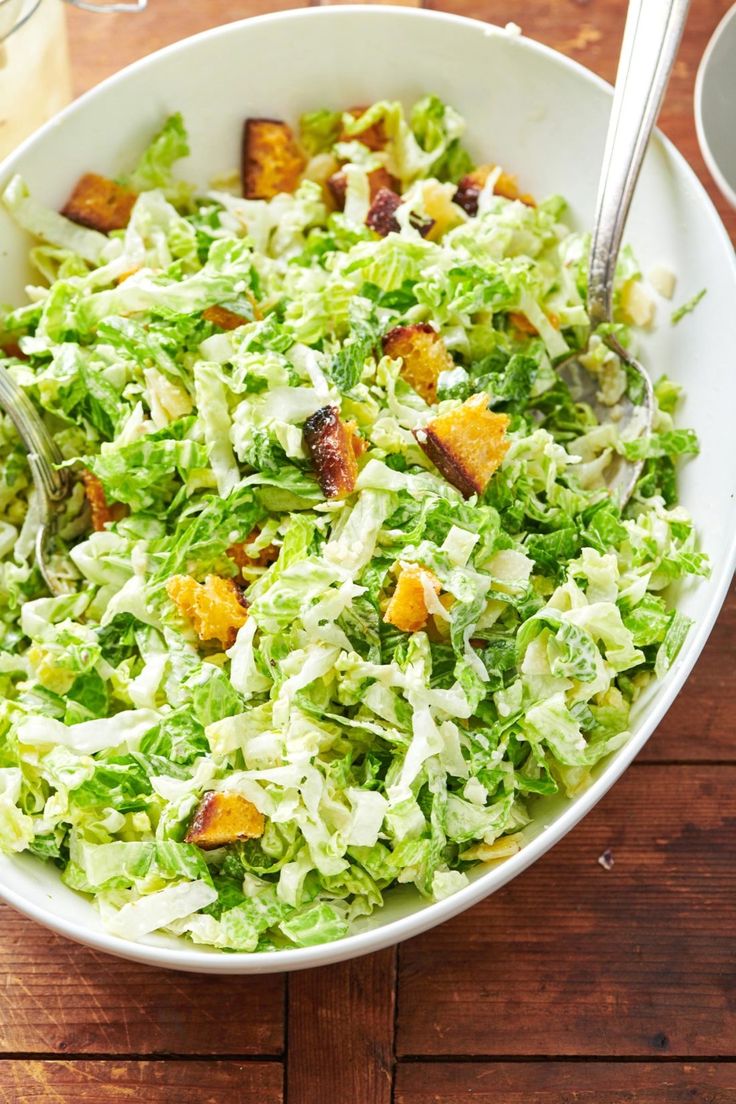 a white bowl filled with lettuce and croutons on top of a wooden table