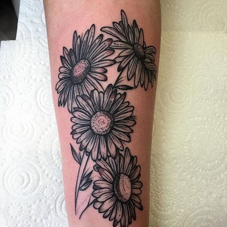 a woman's leg with flowers on it and the caption reads, fineline blackwork bunch of daisies tattoo by gurra