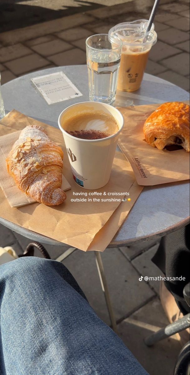 a cup of coffee and some croissants sitting on a table with drinks