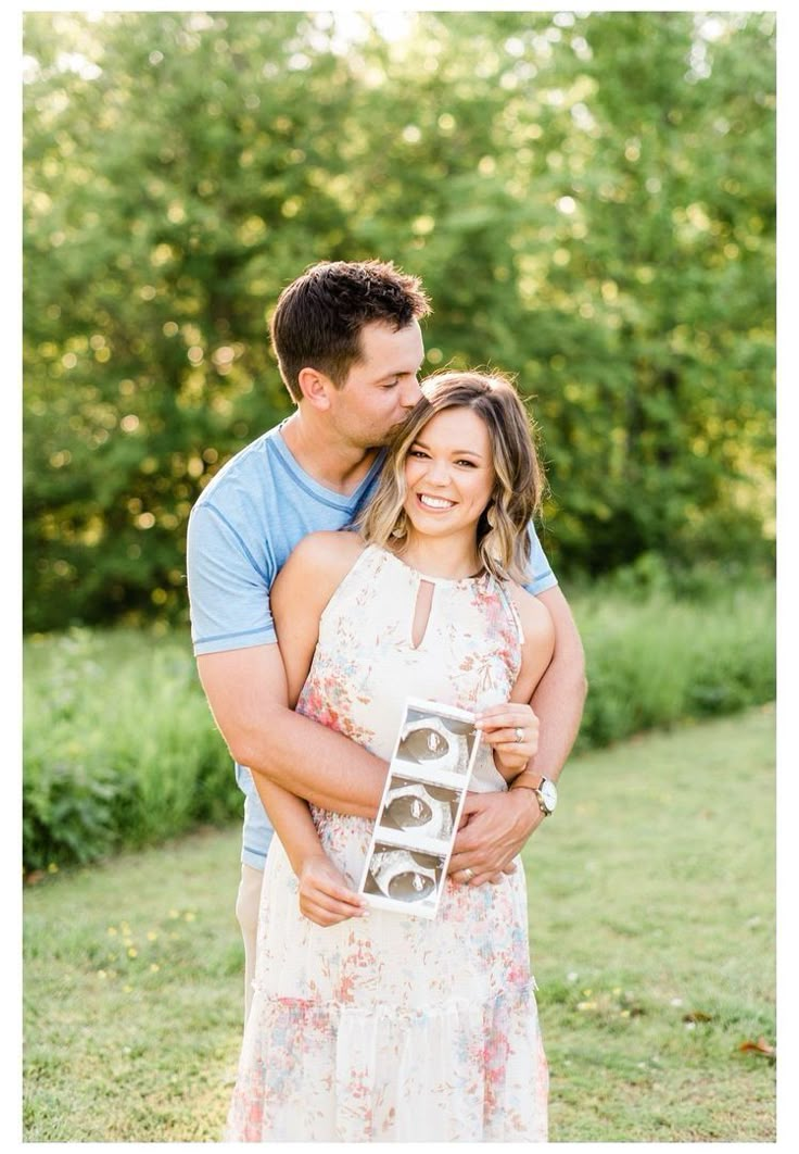 a man and woman hugging each other while holding an object in front of some trees