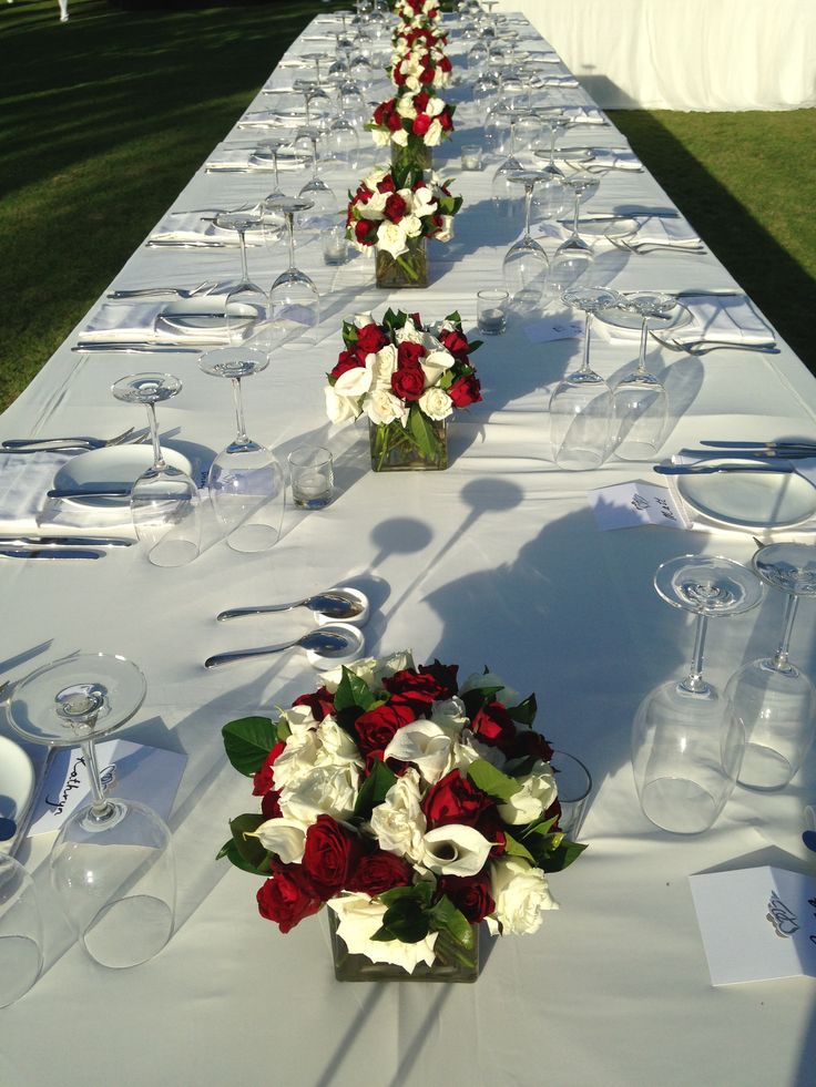 a long table with white and red flowers in vases on top of it's tables