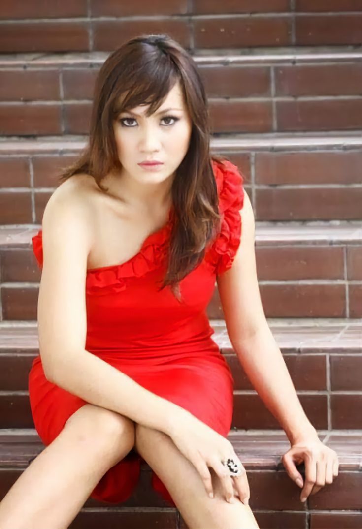 a woman in a red dress is sitting on some steps and posing for the camera