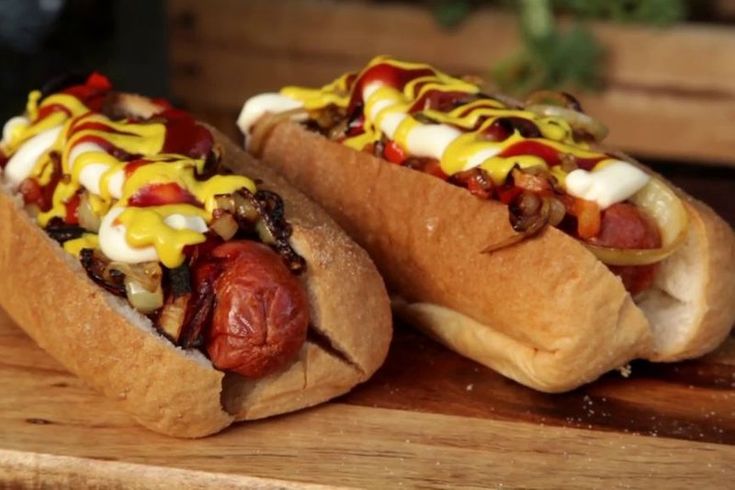 two hotdogs with toppings on them sitting on a wooden table next to each other