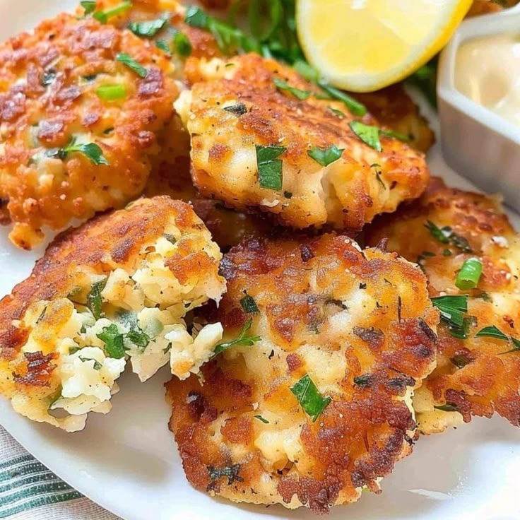 some crab cakes are on a white plate with lemon wedges and lettuce