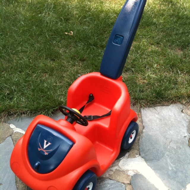 an orange and blue toy car sitting on top of a stone walkway in the grass