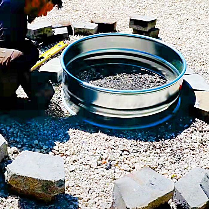 a man kneeling down next to a metal bowl on top of some rocks and gravel