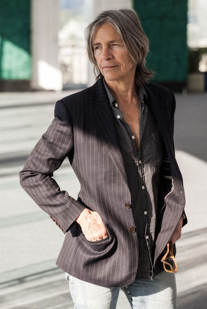 an older woman standing in front of a building with her hands on her hips and looking at the camera