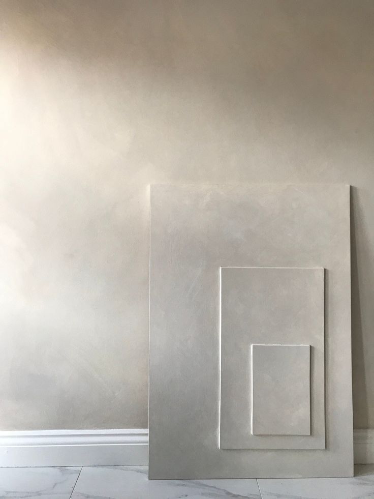 three white square and rectangle shapes against a gray wall in an empty room with marble flooring