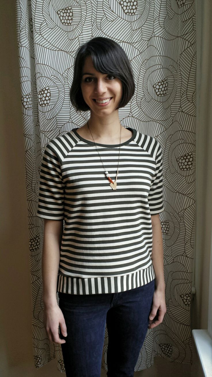 a woman standing in front of a window wearing jeans and a striped shirt with short sleeves