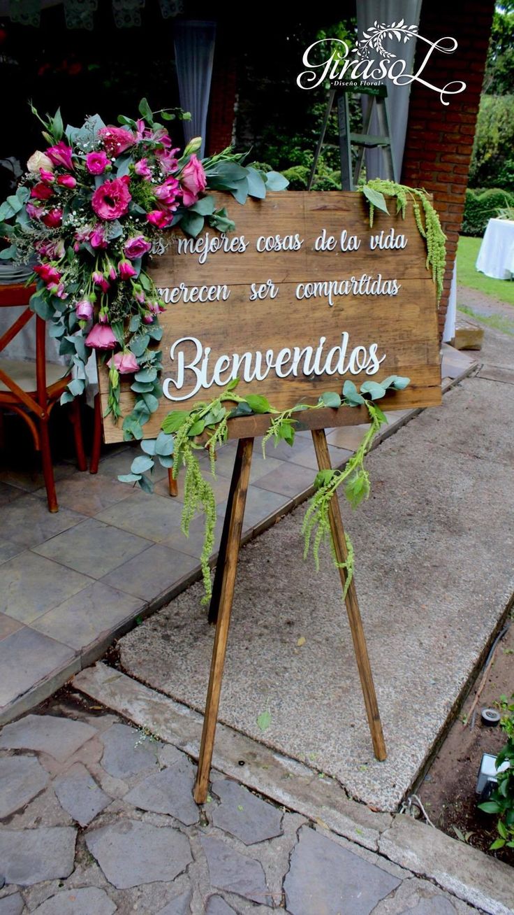 a wooden sign with flowers on it sitting in front of a brick building next to a sidewalk