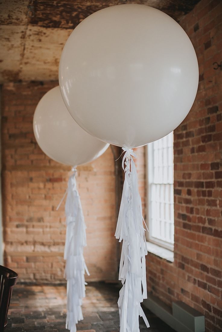 two white balloons with tassels hanging from them in an old brick walled room