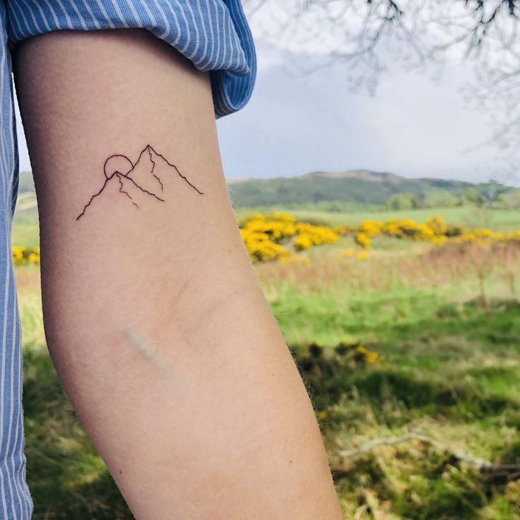 a woman's arm with a tattoo on it that has mountains in the background