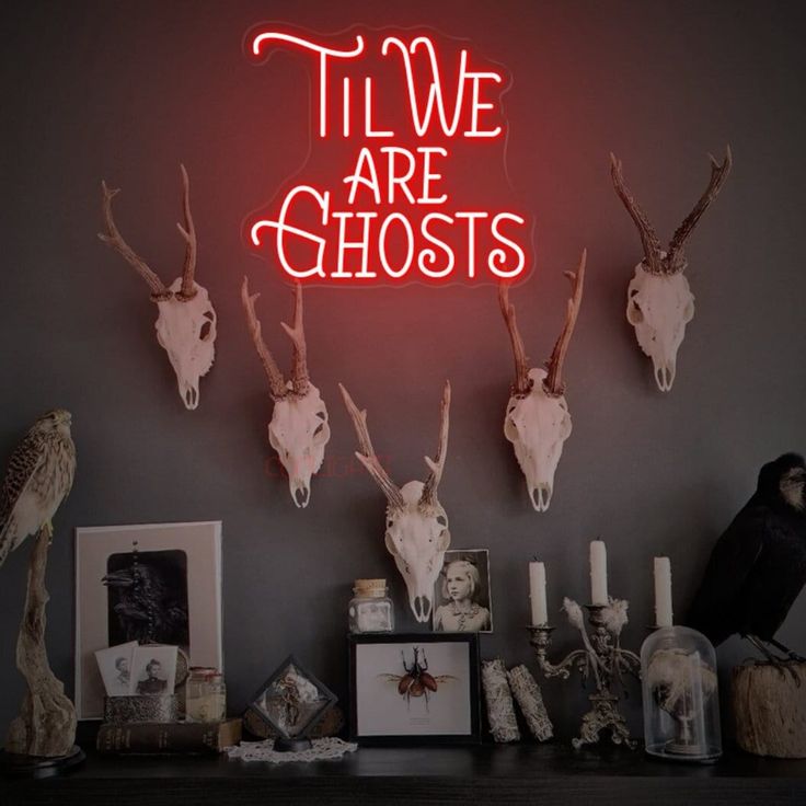 a neon sign that says,'til we are ghosts'with deer heads on the wall