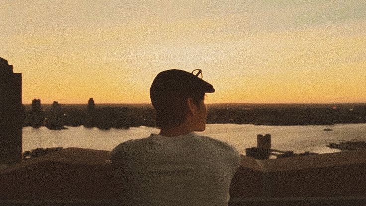 a man sitting on top of a roof looking out at the water and buildings in the distance