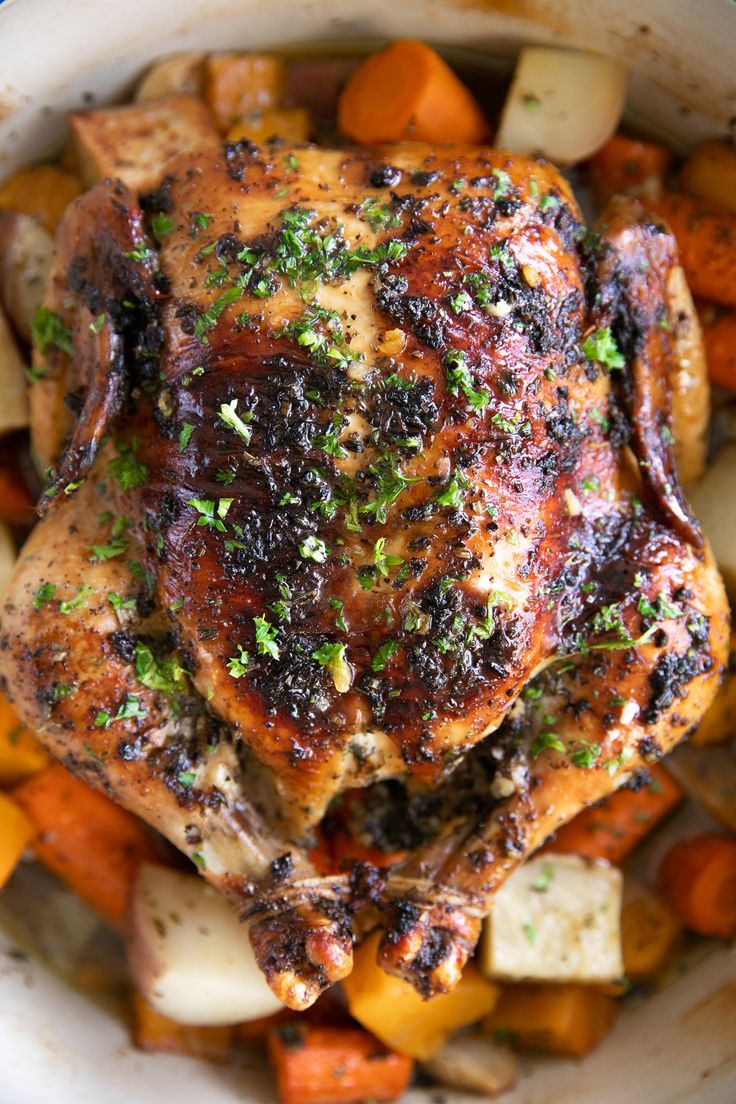 a close up of a chicken in a bowl with carrots, potatoes and parsley