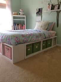 a bedroom with a bed, bookshelf and storage bins